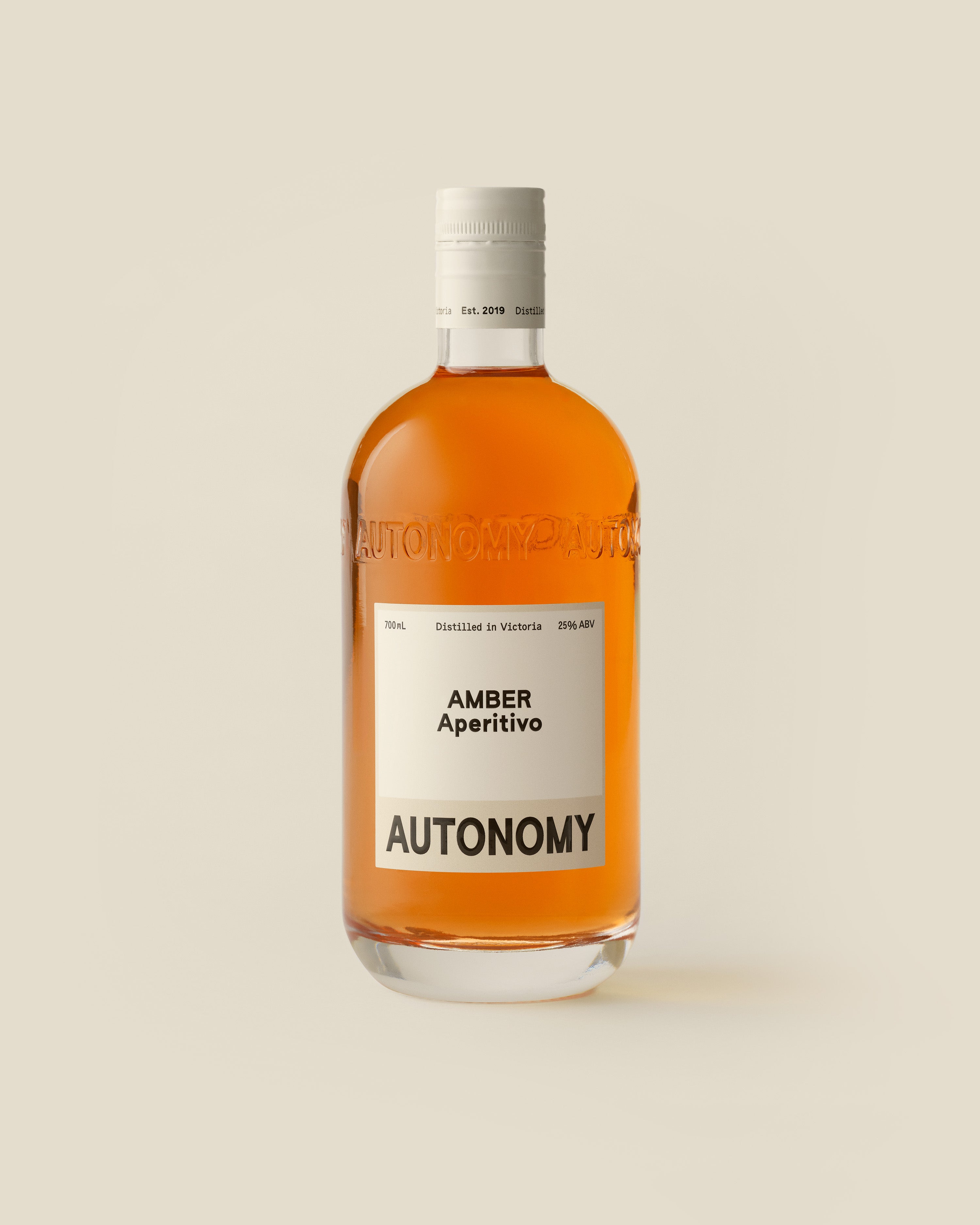 A 700mL bottle of AUTONOMY Amber Aperitivo, featuring a minimalist cream label with black text and debossed AUTONOMY logo on the bottle. The liquid in the bottle is a deep amber colour, and is crafted from gentian, grapefruit, orange and quandong.